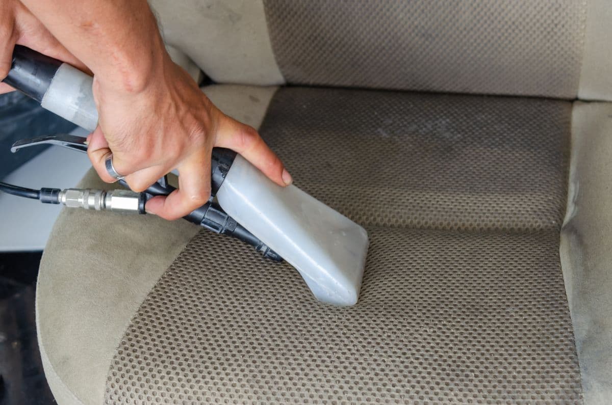 A car seat being deep-cleaned with an upholstery extractor tool